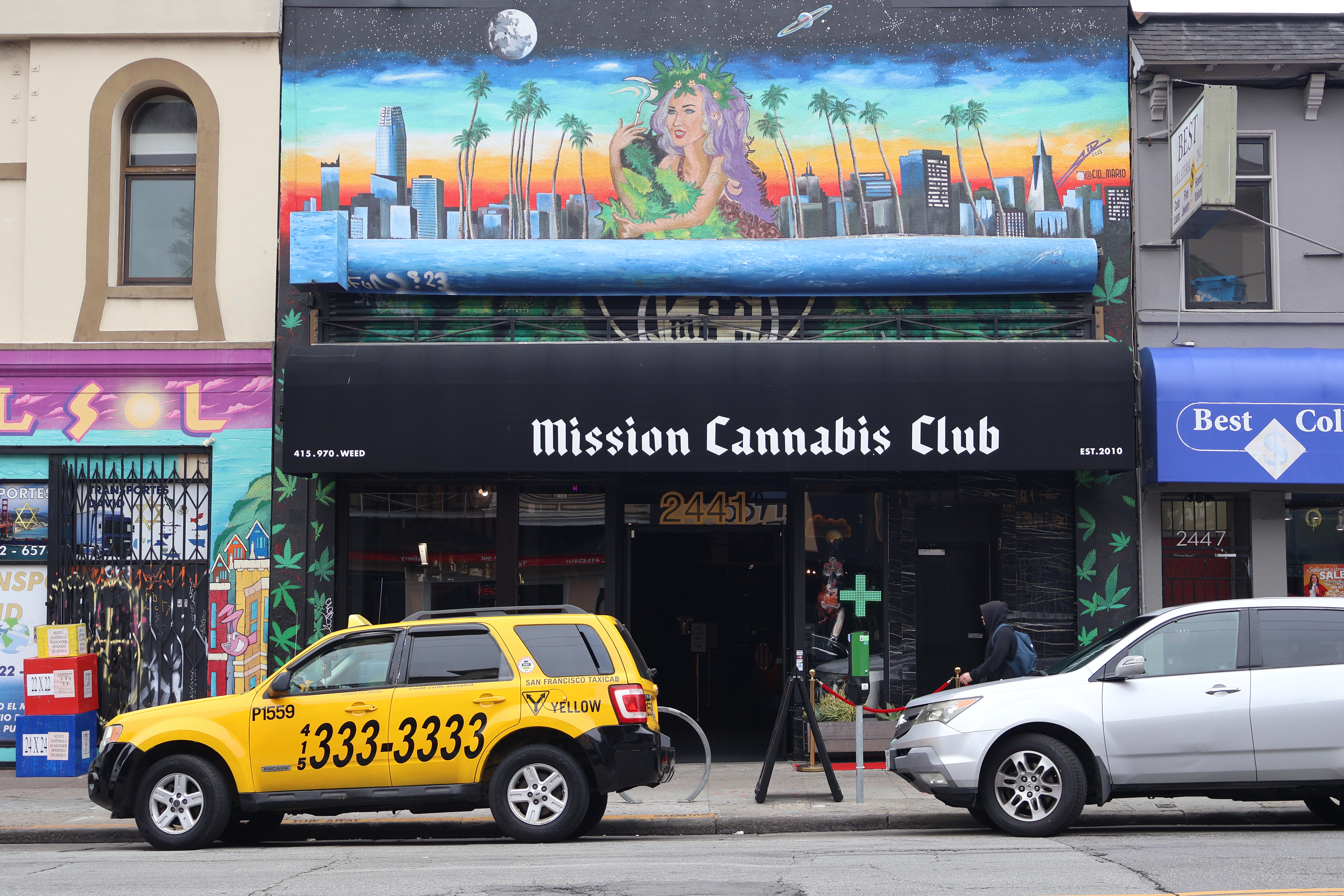 The storefront of Mission Cannabis Club with two cars parked in front of the building